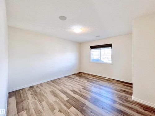 This room features light-colored walls, wood-style flooring, and a window with a dark blind - 17127 7A Avenue, Edmonton, AB - Indoor Photo Showing Other Room
