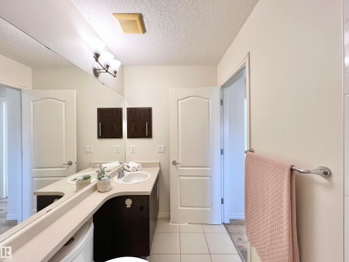 Bathroom featuring a dual sink vanity with dark wood cabinetry, light-colored countertops, and a large mirror - 17127 7A Avenue, Edmonton, AB - Indoor
