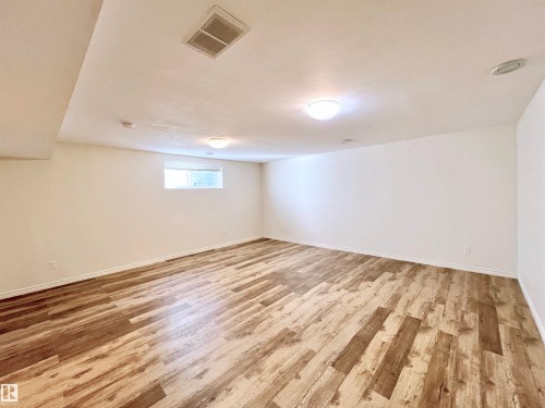 This spacious room features light-toned wood-style flooring, white walls, and a window providing natural light - 17127 7A Avenue, Edmonton, AB - Indoor