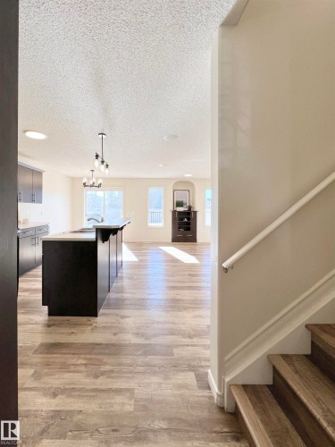 Open-concept living space with wood-look flooring, a kitchen island, and contemporary lighting fixtures - 17127 7A Avenue, Edmonton, AB - Indoor