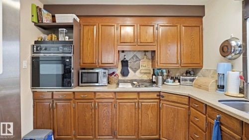 Kitchen featuring wood cabinetry, light-toned countertops, a built-in wall oven, and a patterned tile backsplash - 10922 117 Street, Edmonton, AB - Indoor Photo Showing Kitchen