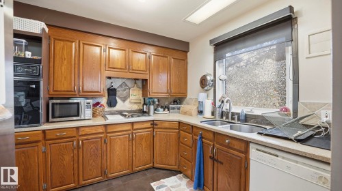 The kitchen features wood cabinetry, light-colored countertops, a double basin sink, and a built-in oven and microwave - 10922 117 Street, Edmonton, AB - Indoor Photo Showing Kitchen With Double Sink