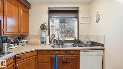 The kitchen features wood cabinetry, a double basin sink, a dishwasher, and a window with a valance - 10922 117 Street, Edmonton, AB - Indoor Photo Showing Kitchen With Double Sink