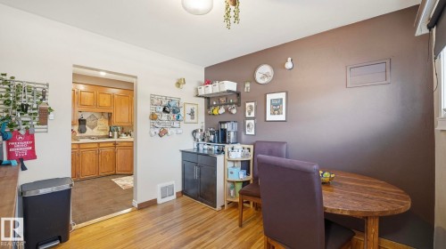 The property features hardwood floors and a dining area with a wooden table and chairs, leading into a kitchen with wood cabinetry and dark flooring - 10922 117 Street, Edmonton, AB - Indoor