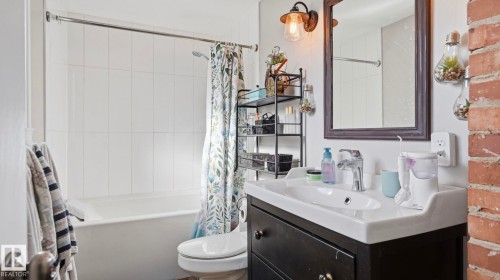 Bathroom featuring white subway tile surround for the bathtub, a vanity with a white basin and dark cabinetry, and an exposed brick wall accent - 10922 117 Street, Edmonton, AB - Indoor Photo Showing Bathroom