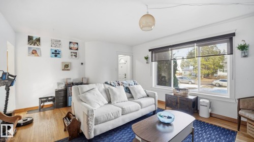 The living room features hardwood flooring, white walls, and a large window with roller shades - 10922 117 Street, Edmonton, AB - Indoor Photo Showing Living Room