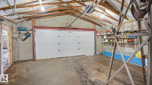 The property includes a spacious garage with a white overhead door, concrete flooring, and exposed ceiling beams - 10922 117 Street, Edmonton, AB - Indoor Photo Showing Garage