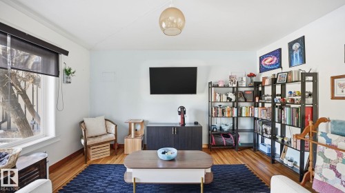Living area with light-colored walls, hardwood flooring, and a large window providing natural light - 10922 117 Street, Edmonton, AB - Indoor