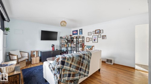 Living area featuring hardwood flooring, light-colored walls, and a window with a roller shade - 10922 117 Street, Edmonton, AB - Indoor