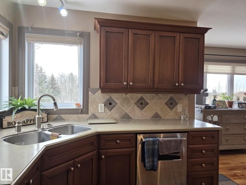 The kitchen features dark wood cabinetry, a double basin sink with a brushed nickel faucet, light-colored countertops, and a tiled backsplash with diamond accents - 4477 36 Street, Drayton Valley, AB - Indoor Photo Showing Kitchen With Double Sink