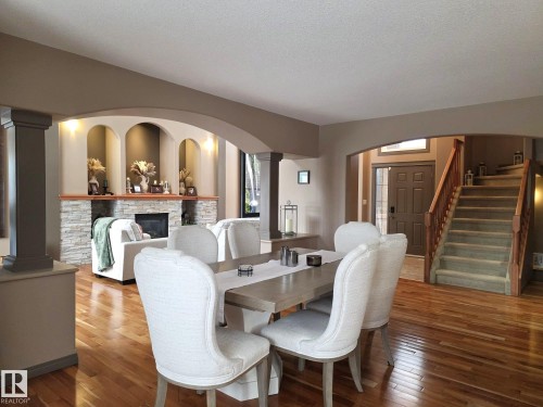 Bright and inviting interior featuring hardwood flooring, a stone fireplace, and an elegant staircase with wood banisters - 4477 36 Street, Drayton Valley, AB - Indoor Photo Showing Dining Room