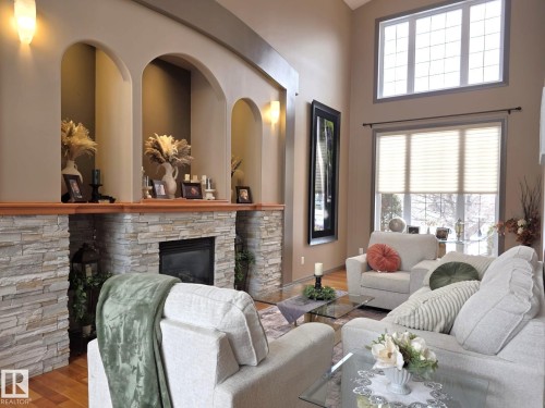Living area featuring a stone-clad fireplace with a wooden mantel, arched display niches, and high ceilings with large windows providing natural light - 4477 36 Street, Drayton Valley, AB - Indoor Photo Showing Living Room With Fireplace