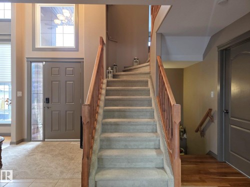 Foyer featuring a grand staircase with carpeted treads and wooden railings, a front door with a decorative glass sidelight, and a large window above the entrance providing ample natural light - 4477 36 Street, Drayton Valley, AB - Indoor Photo Showing Other Room