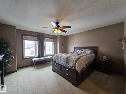 This room features soft carpeting, a ceiling fan with light fixture, and two large windows with blinds and curtains - 4477 36 Street, Drayton Valley, AB - Indoor Photo Showing Bedroom