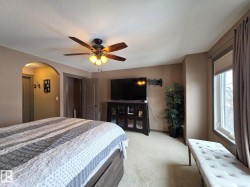 This bedroom features a ceiling fan with light fixture, carpeted flooring, and a large window with blinds and drapes - 