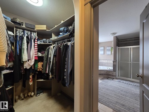 Expansive walk-in closet with built-in shelving, hanging rods, and carpeted flooring, providing direct access to a bathroom featuring a corner bathtub and a glass-enclosed shower - 4477 36 Street, Drayton Valley, AB - Indoor With Storage