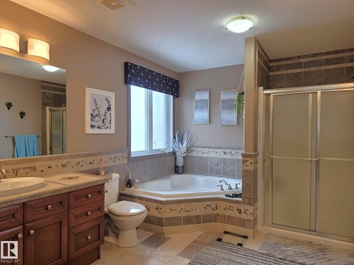 This bathroom features a spacious corner soaking tub, a separate shower with frosted glass doors, and a vanity with rich wood cabinetry and a rectangular sink - 4477 36 Street, Drayton Valley, AB - Indoor Photo Showing Bathroom
