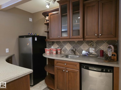 This space features rich wood cabinetry with both solid and glass-front doors, a countertop with an integrated sink and faucet, and a tiled backsplash - 4477 36 Street, Drayton Valley, AB - Indoor Photo Showing Kitchen