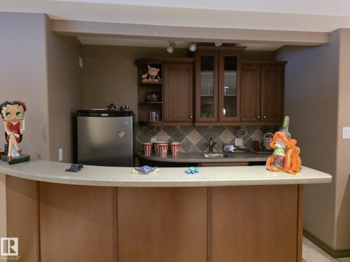 This property features a wet bar with wood cabinetry, a stainless steel compact refrigerator, a sink, and a tiled backsplash - 4477 36 Street, Drayton Valley, AB - Indoor Photo Showing Kitchen