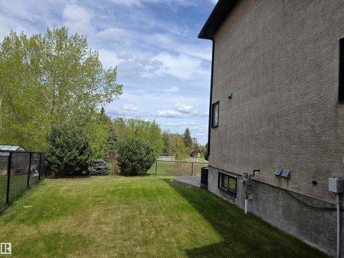 Expansive green lawn surrounded by mature trees, featuring a chain-link fence and a stucco exterior - 4477 36 Street, Drayton Valley, AB - Outdoor