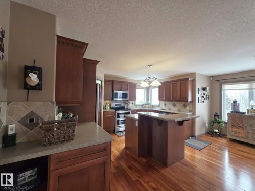 The kitchen features extensive wooden cabinetry, a central island with a breakfast bar, stainless steel appliances, and hardwood floors - 4477 36 Street, Drayton Valley, AB - Indoor Photo Showing Kitchen