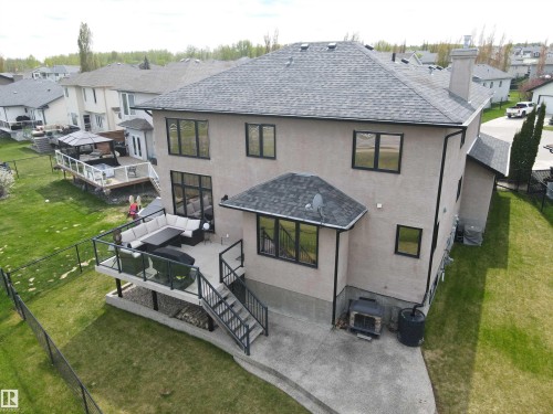 Rear exterior featuring a multi-level deck with black railing and glass panels, a concrete patio, and a shingled roof - 4477 36 Street, Drayton Valley, AB - Outdoor