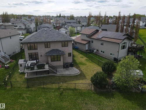 Rear exterior featuring a black chain-link fence enclosing a green lawn, two-story design, large windows, and an elevated deck with dark railings - 4477 36 Street, Drayton Valley, AB - Outdoor