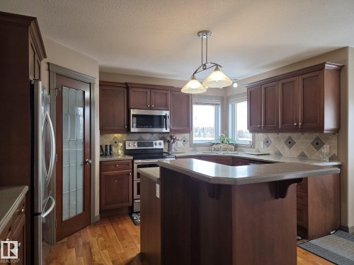 The kitchen features rich wood cabinetry, stainless steel appliances, and a central island with a breakfast bar - 4477 36 Street, Drayton Valley, AB - Indoor Photo Showing Kitchen