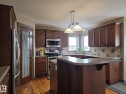 The kitchen features rich wood cabinetry, stainless steel appliances, and a central island with a breakfast bar - 