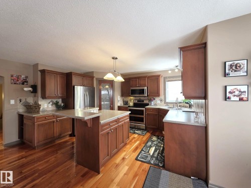 The kitchen features rich wood cabinetry, stainless steel appliances, light-colored countertops, hardwood flooring, and an island with an extended counter - 4477 36 Street, Drayton Valley, AB - Indoor Photo Showing Kitchen