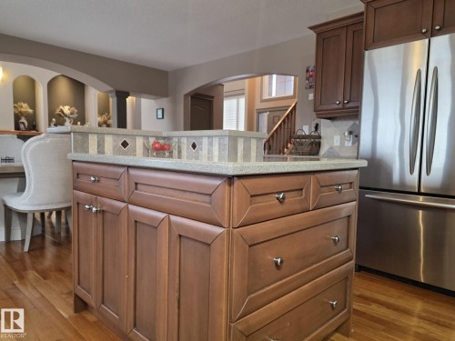 The kitchen features a center island with a tiled backsplash and light-colored countertop, along with wooden cabinetry and a stainless steel refrigerator - 4477 36 Street, Drayton Valley, AB - Indoor Photo Showing Kitchen