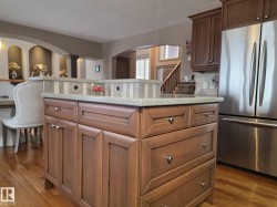 The kitchen features a center island with a tiled backsplash and light-colored countertop, along with wooden cabinetry and a stainless steel refrigerator - 