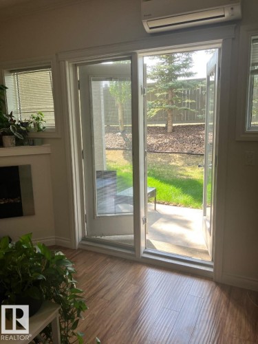 The property features hardwood floors, a wall-mounted air conditioning unit, and a glass paneled door that opens to an outdoor patio area with a fenced yard - 145 10121 80 Avenue, Edmonton, AB - Indoor Photo Showing Other Room