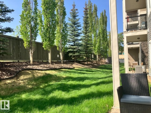 The property features a private patio area with an air conditioning unit and a view of the manicured lawn - 145 10121 80 Avenue, Edmonton, AB - Outdoor