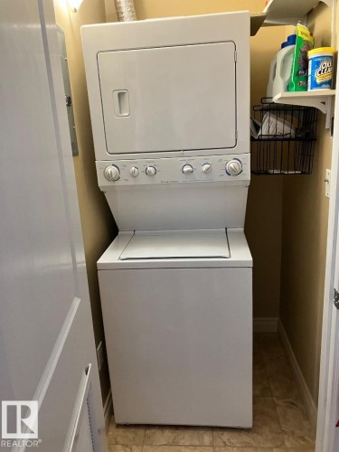 Dedicated laundry area featuring a stacked washer and dryer unit, tiled flooring, and a wall-mounted shelf - 145 10121 80 Avenue, Edmonton, AB - Indoor Photo Showing Laundry Room