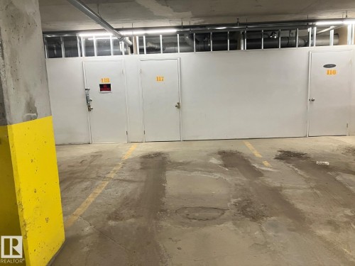 The property offers dedicated storage units with white doors and visible numbering, alongside marked parking spaces on a concrete floor - 145 10121 80 Avenue, Edmonton, AB - Indoor Photo Showing Garage