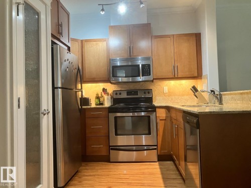 The kitchen features stainless steel appliances, wood cabinetry, granite countertops, and a tile backsplash - 145 10121 80 Avenue, Edmonton, AB - Indoor Photo Showing Kitchen With Stainless Steel Kitchen