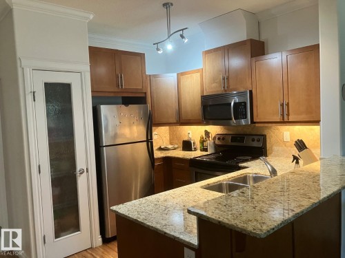 The kitchen features wood cabinetry, stainless steel appliances, granite countertops, and a double basin sink - 145 10121 80 Avenue, Edmonton, AB - Indoor Photo Showing Kitchen With Stainless Steel Kitchen With Double Sink With Upgraded Kitchen