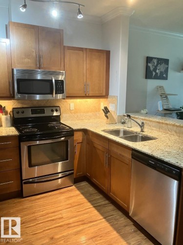 The kitchen features stainless steel appliances, including an oven, microwave, and dishwasher, complemented by wood cabinetry and granite countertops - 145 10121 80 Avenue, Edmonton, AB - Indoor Photo Showing Kitchen With Stainless Steel Kitchen With Double Sink