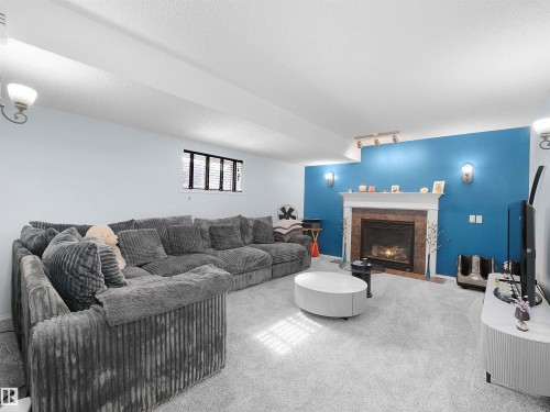 Living area featuring a fireplace with a stone surround and a white mantel, light gray carpeting, and a window with horizontal blinds - 13040 34 Street, Edmonton, AB - Indoor Photo Showing Living Room With Fireplace