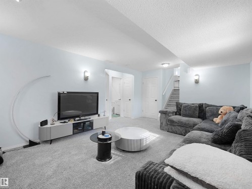 This living space features light blue walls, sconce lighting, and soft grey carpeting throughout - 13040 34 Street, Edmonton, AB - Indoor Photo Showing Living Room