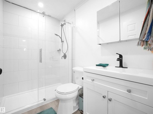 This bathroom features a contemporary vanity with a white countertop and base, a black faucet, and a mirrored medicine cabinet - 13040 34 Street, Edmonton, AB - Indoor Photo Showing Bathroom