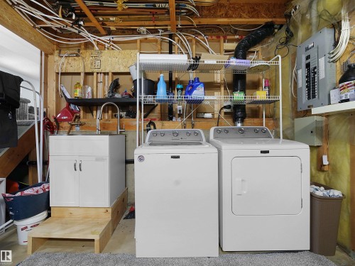 Dedicated laundry area featuring a white washing machine and dryer, a utility sink with cabinet storage, and exposed ceiling joists - 13040 34 Street, Edmonton, AB - Indoor Photo Showing Laundry Room