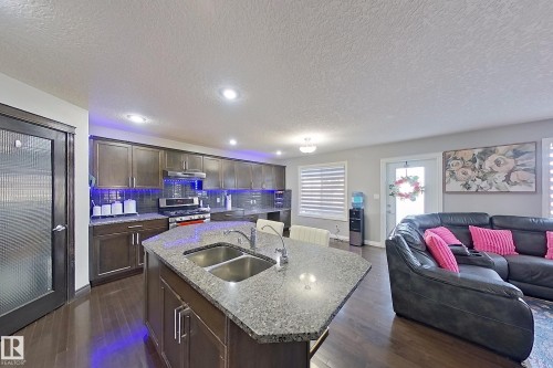 Open-concept living space with dark wood flooring, a kitchen featuring dark cabinetry, stainless steel appliances, and an island with a double sink, and a comfortable lounge area - 1743 60 Street Sw, Edmonton, AB - Indoor Photo Showing Other Room