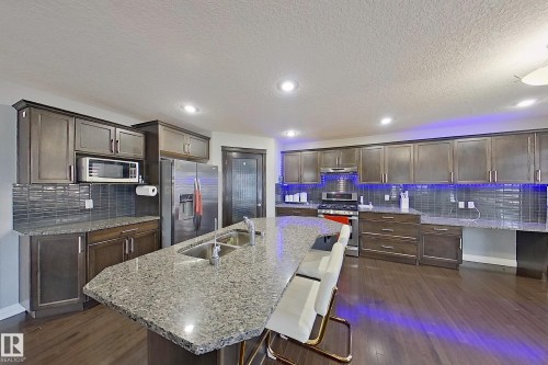 The kitchen features dark wood cabinetry, a large kitchen island with a double sink and granite countertops, and stainless steel appliances - 1743 60 Street Sw, Edmonton, AB - Indoor Photo Showing Kitchen With Double Sink With Upgraded Kitchen