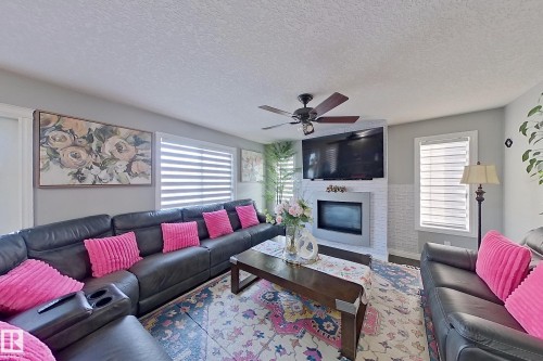 Spacious living area featuring a fireplace with a decorative mantel, a ceiling fan, and window blinds - 1743 60 Street Sw, Edmonton, AB - Indoor Photo Showing Living Room With Fireplace