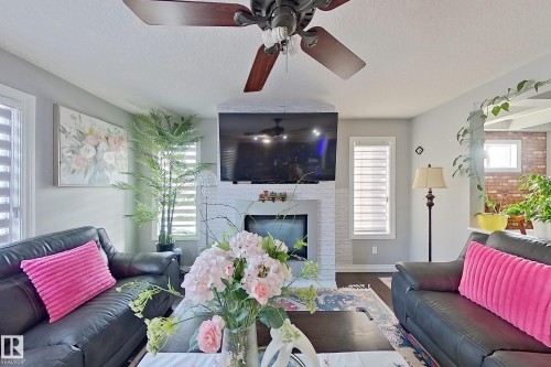 Living area featuring a ceiling fan with dark wood blades, a white brick fireplace, and windows with horizontal blinds - 1743 60 Street Sw, Edmonton, AB - Indoor Photo Showing Living Room With Fireplace