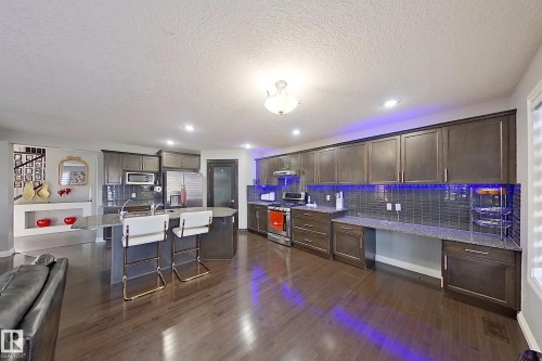 The kitchen features extensive dark wood cabinetry, a tiled backsplash, and stainless steel appliances - 1743 60 Street Sw, Edmonton, AB - Indoor Photo Showing Other Room