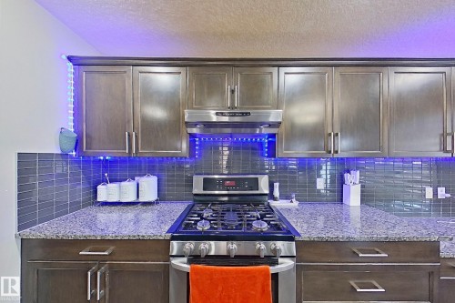 The kitchen features dark wood cabinetry, granite countertops, and a subway tile backsplash - 1743 60 Street Sw, Edmonton, AB - Indoor Photo Showing Kitchen