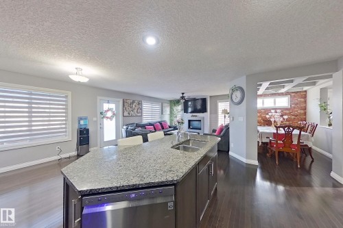 The property features an open concept layout with dark hardwood floors, a kitchen island with a double sink and granite countertops, and a dining area with exposed brick accents - 1743 60 Street Sw, Edmonton, AB - Indoor Photo Showing Kitchen With Double Sink